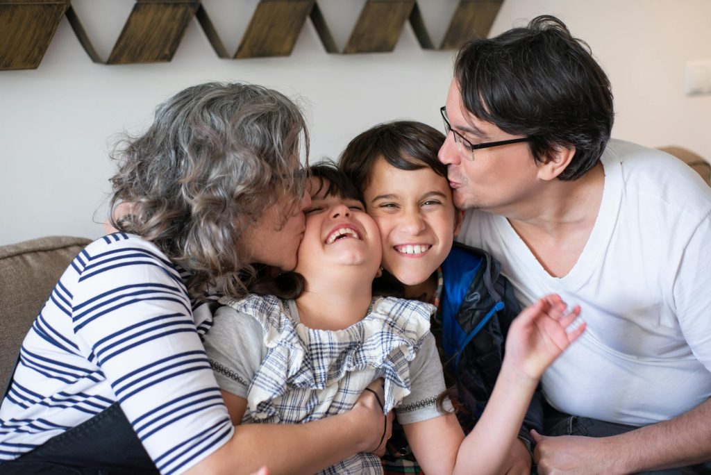 A joyful family moment with parents kissing their smiling children indoors.